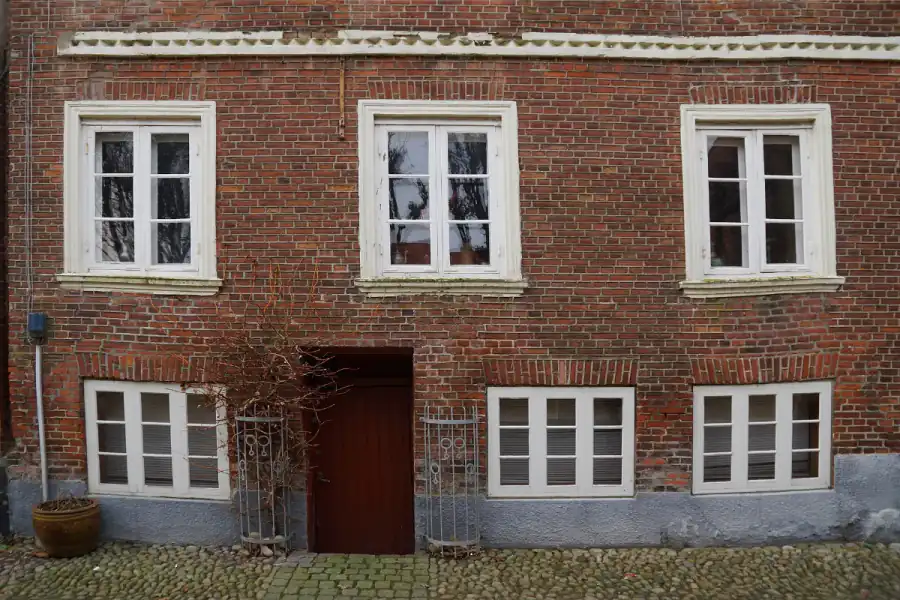 Old brick house front where the window sills, lintels and brick courses slope downward toward one side after differential settlement
