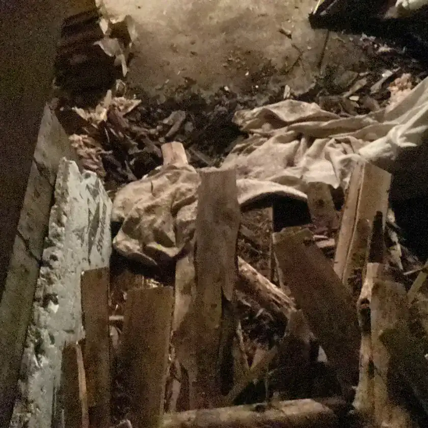 Dark view into the collapsed basement of an old house, with broken boards, fallen debris and soil filling the space