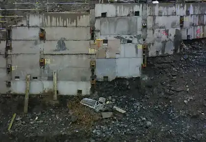 Sections of new poured concrete underpinning below an old stone wall, with soil excavated in front