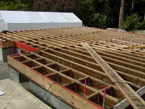 New floor framing of engineered I-joists resting on a sill plate on a concrete foundation wall, with rim boards and blocking, before the subfloor goes down