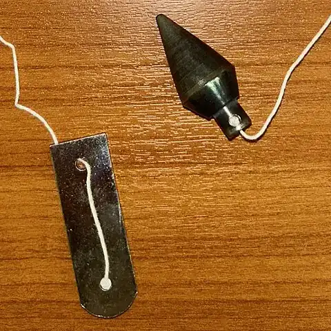 Steel plumb bob on a length of white string beside a small metal holder on a wooden surface