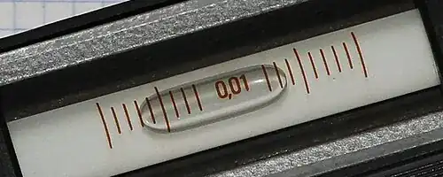 Close view of the bubble vial on a precision spirit level, with graduated marks on either side of the bubble