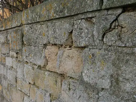 Close view of a limestone wall bulging outward with blocks opening at the mortar joints and a crack near the top course