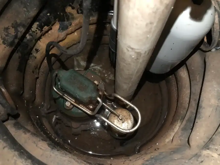 Submersible sump pump with a float switch sitting in water at the bottom of a basement sump pit, with the discharge pipe rising out of the pit