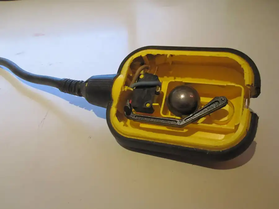 Yellow tethered float switch cut open to show a steel ball and lever that press a small microswitch when the float tips up