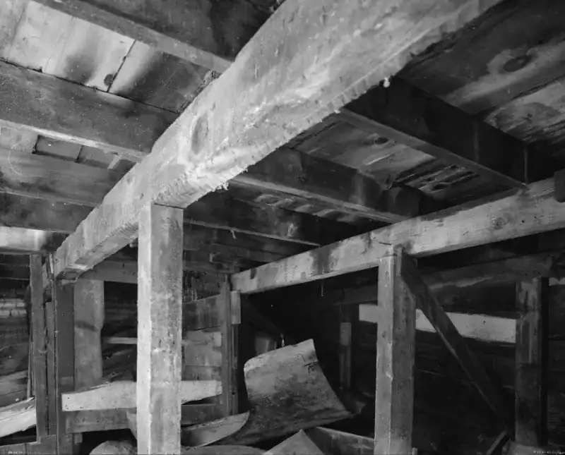 Black and white photo of wood posts and beams with a diagonal brace carrying the floor joists under an old house